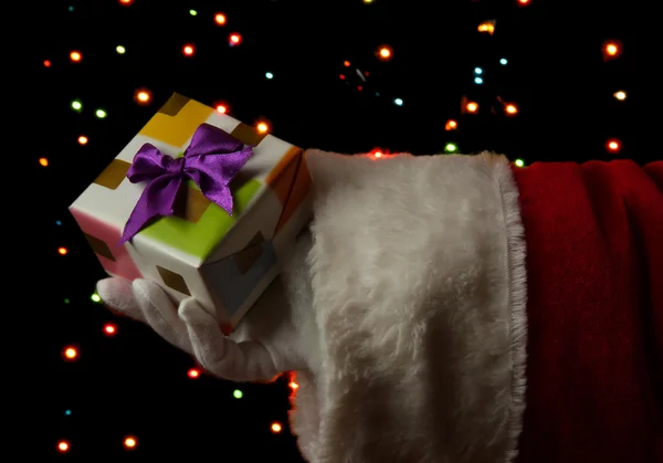 Santa Claus hand holding gift box on bright background — Stock Photo, Image