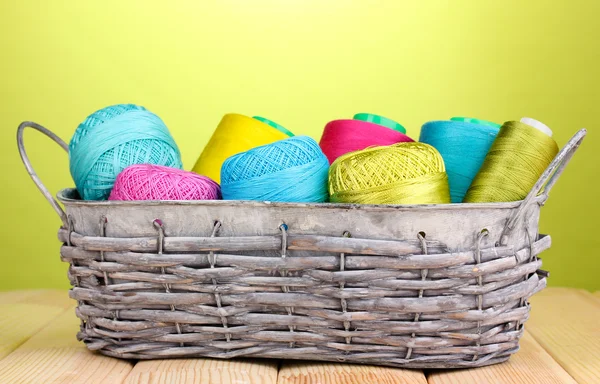 Bright threads in basket on wooden table on green background — Stock Photo, Image