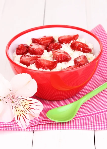 Hüttenkäse in roter Schüssel mit Erdbeerscheiben auf weißem Holztisch — Stockfoto