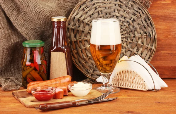 Bière et saucisses grillées sur table en bois sur fond de sac — Photo