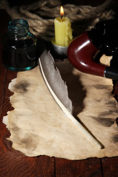 Старая бумага с чернилами возле зажигания свечи на деревянном столе — стоковое фото