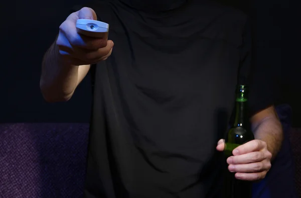 Człowiek ręki trzymającej telewizor, pilot zdalnego sterowania i butelki piwa, na ciemnym tle — Zdjęcie stockowe