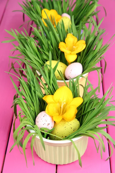 Ovos de Páscoa em tigelas com grama na mesa de madeira rosa de perto — Fotografia de Stock