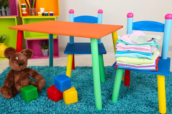 Mesa pequena e colorida e cadeiras com roupas de bebê — Fotografia de Stock