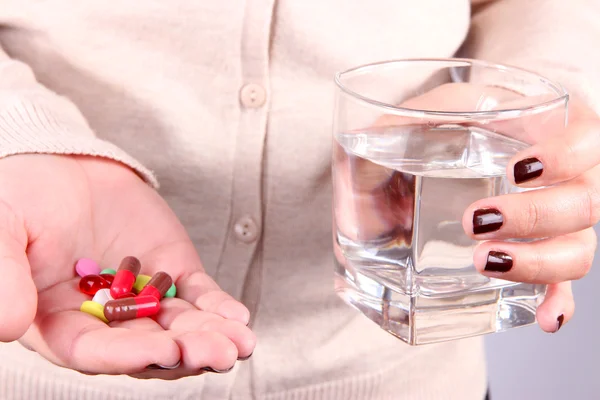 Muchas píldoras y agua de vidrio en la mano — Foto de Stock