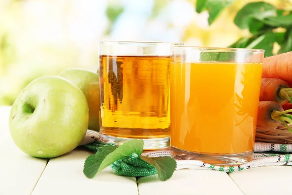 Ποτήρια χυμό, τα μήλα και τα καρότα στην λευκό ξύλινο τραπέζι, σε πράσινο φόντο — Φωτογραφία Αρχείου