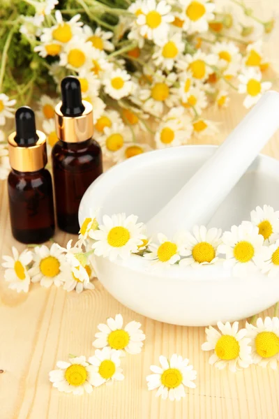 Aceite esencial y flores de manzanilla en mortero sobre mesa de madera —  Fotos de Stock