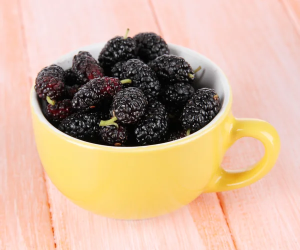 Ripe mulberries in cup on wooden background — Stock Photo, Image