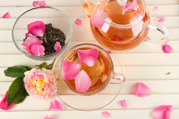 Kettle and cup of tea from tea rose on wooden background — Stock Photo, Image