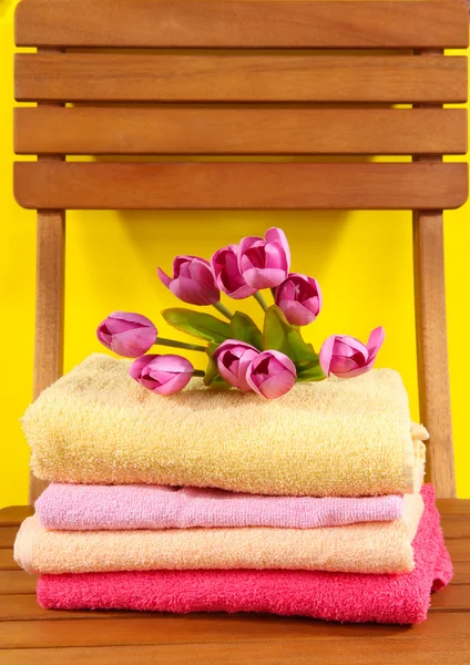 Toallas y flores en silla de madera sobre fondo amarillo — Foto de Stock