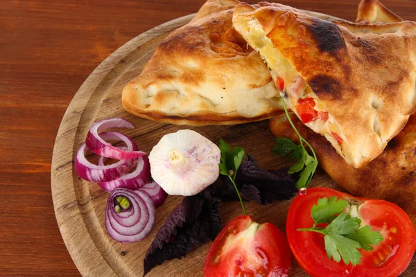 Pizza calzones on wooden board on wooden table — Stock Photo, Image