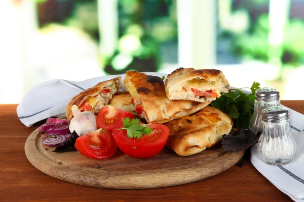 Pizza calzones on wooden board near napkin on wooden table on window background — Stock Photo, Image