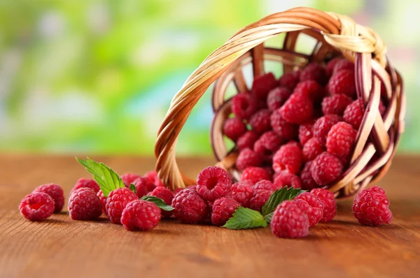 Reife süße Himbeeren im Korb auf Holztisch, auf grünem Hintergrund — Stockfoto