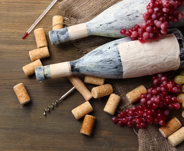 Garrafas velhas de vinho, uvas e rolhas sobre fundo de madeira — Fotografia de Stock