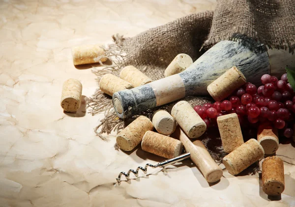 Vieja botella de vino, uvas y corchos sobre fondo de papel viejo —  Fotos de Stock