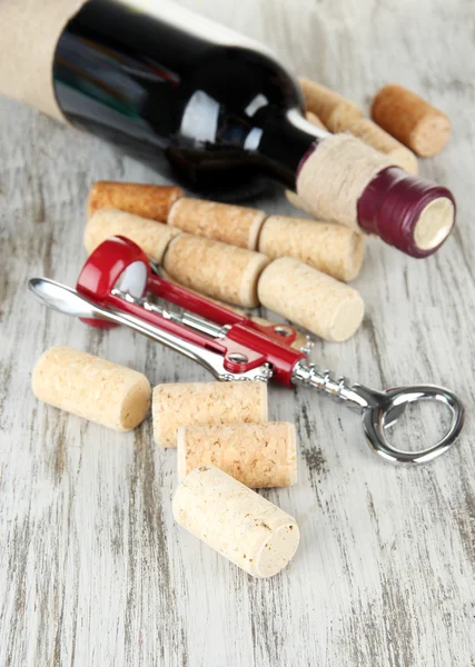 Corkscrew with wine corks and bottle of wine on wooden table close-up — Stock Photo, Image