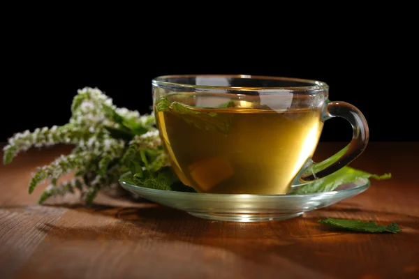 Чашка травяного чая со свежими мятными цветами на деревянном столе на черном фоне — стоковое фото