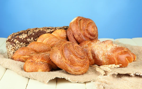 Composition with bread, rolls on sackcloth, on wooden table, on color background — Stock Photo, Image