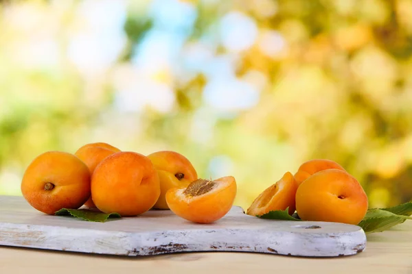Apricots on board on wooden table on nature background — Stock Photo, Image