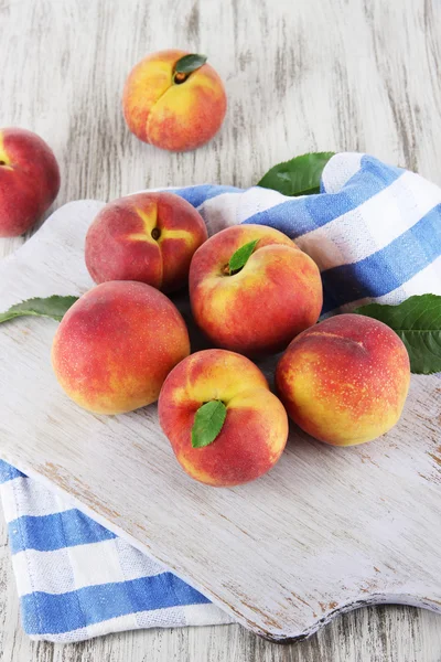 Peaches on board on napkin on table on wooden background — Stock Photo, Image