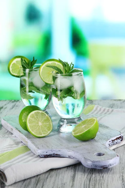 Glasses of cocktail with ice on board on napkin on wooden table on room background — Stock Photo, Image