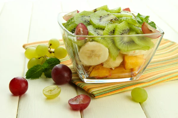 Smakelijke fruitsalade in glazen kom, op witte houten tafel — Stockfoto