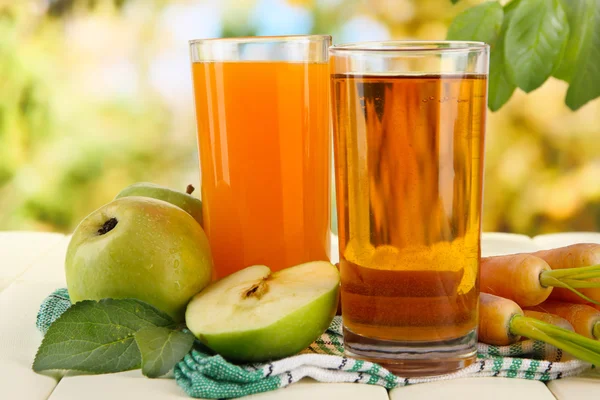 Bicchieri di succo, mele e carote su tavolo di legno bianco, su sfondo verde — Foto Stock