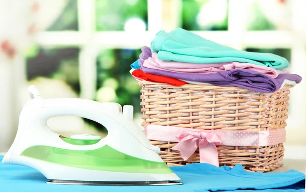 Steam iron and wicker basket with clothes, on bright background — Stock Photo, Image