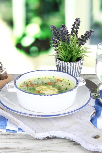 Soupe dans une assiette sur une serviette sur une planche en bois sur fond de fenêtre — Photo