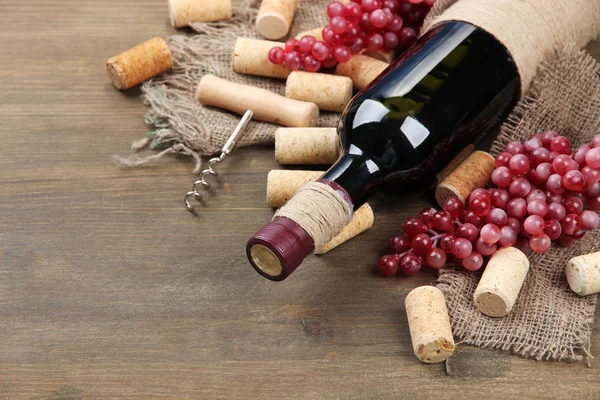 Bottiglia di vino, uva e tappi su fondo di legno — Foto Stock