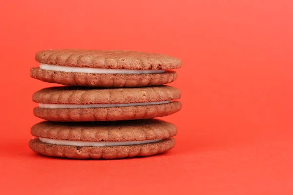 Kırmızı zemin üzerine krem tabakası ile çikolatalı kurabiye — Stok fotoğraf