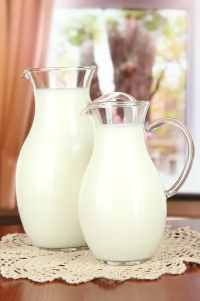 Pitchers of milk on table in room — Stock Photo, Image