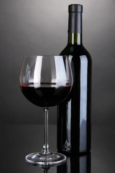 Rood glas wijn en een fles wijn op de grijze achtergrond — Stockfoto