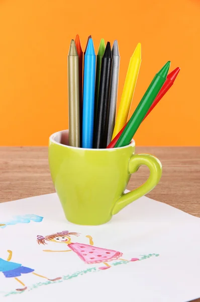 Barevné tužky v poháru na tabulce na oranžovém pozadí — Stock fotografie