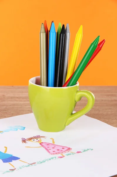 Colorful pencils in cup on table on orange background