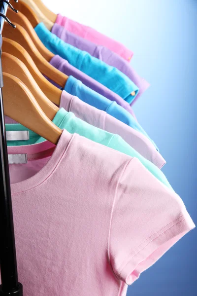 Lots of T-shirts on hangers on blue background — Stock Photo, Image