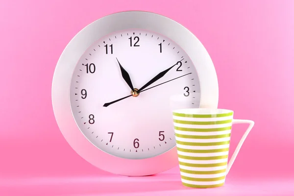 Šálek čaje a hodiny na růžovém pozadí — Stock fotografie