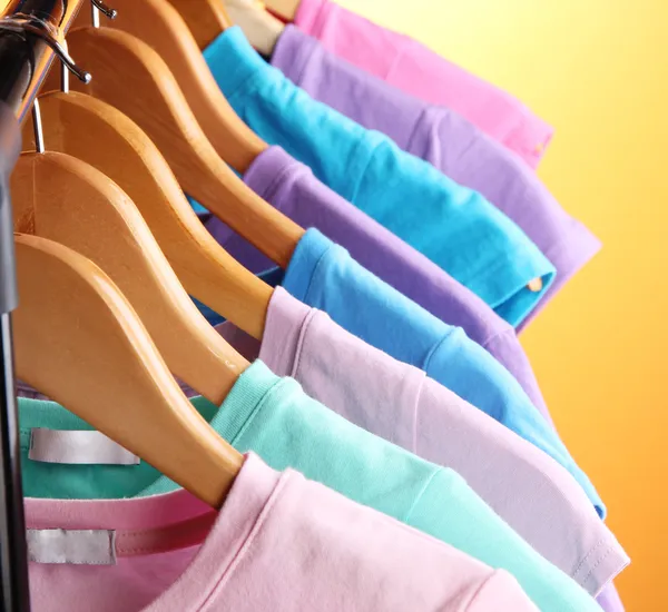 Lots of T-shirts on hangers on orange background — Stock Photo, Image