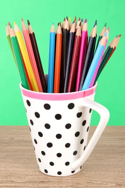 Colorful pencils in cup on table on green background — Stock Photo, Image