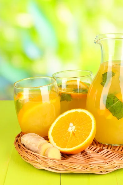 Оранжевый лимонад в кувшине и стаканы на деревянном столе на естественном фоне — стоковое фото