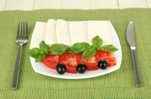 Сыр из овечьего молока, с базиликом и помидорами на цветной салфетке на деревянном фоне — стоковое фото