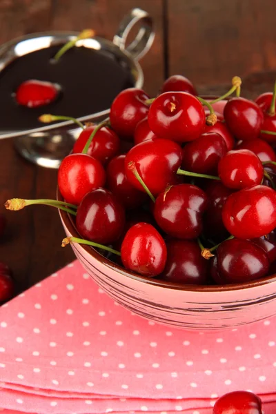 Спелые красные ягоды вишни в миске и шоколадный соус на деревянном столе крупным планом — стоковое фото