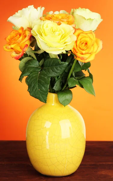 Hermoso ramo de rosas en jarrón sobre la mesa sobre fondo naranja — Foto de Stock