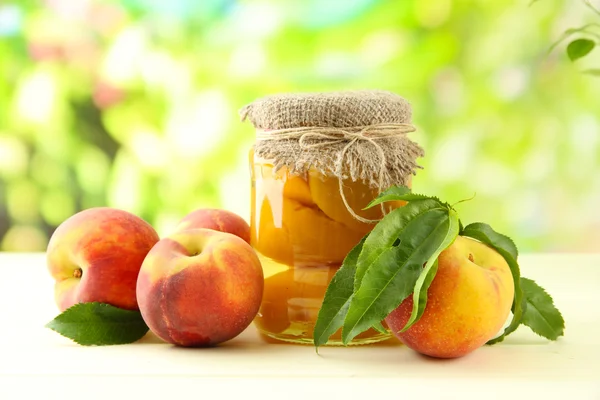 Jar of canned peaches and fresh peaches on wooden table, outside