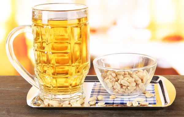 Beer in glass and nuts on tray on wooden table on room background — Stock Photo, Image