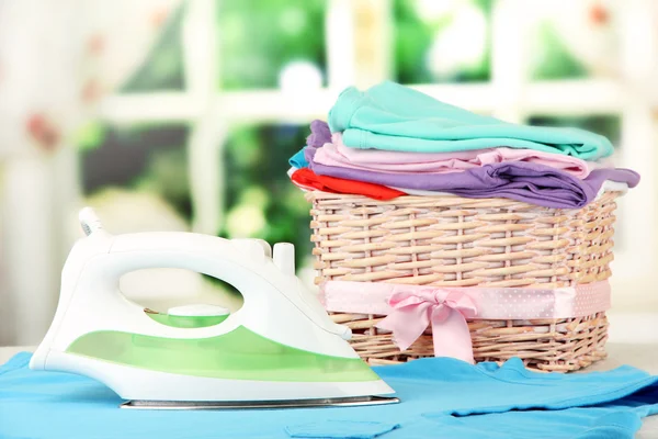 Steam iron and wicker basket with clothes, on bright background — Stock Photo, Image