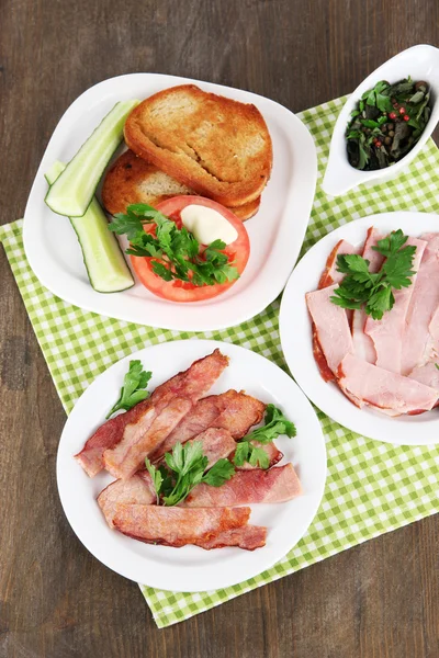 Bacon på tallrikar på servett på träbord — Stockfoto