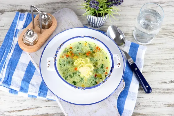 Soupe dans une assiette sur une serviette sur une planche en bois sur une table — Photo