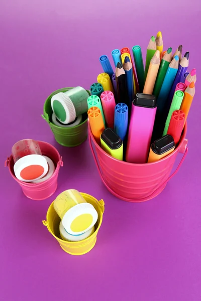 गौचे पेंट, पेन और बैंगनी पृष्ठभूमि पर टोकरी में विभिन्न रंगों के मार्कर — स्टॉक फ़ोटो, इमेज