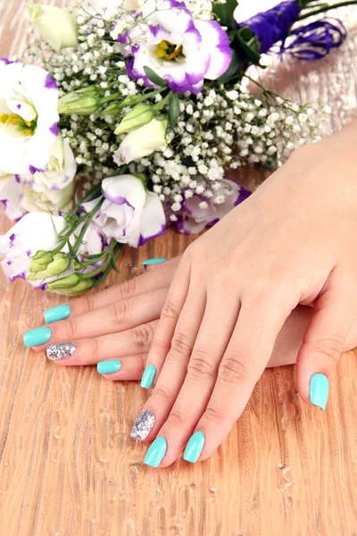 Beautiful woman hands with blue manicure near bouquet of beautiful flowers, on color background — Stock Photo, Image